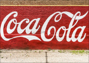 An old, painted Coca-Cola sign on the side of a bu