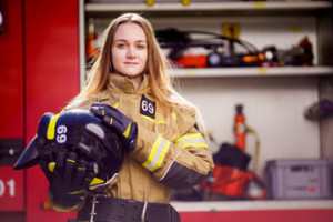 Fototapeta Straż Photo of woman firefighter with helmet in her hands standing near fire truck