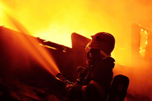 Fototapeta Straż A firefighter sprays water from a hose into a flames during a night fire