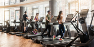 Fototapeta Siłownia Group of four people, men and women, running on treadmills in modern and luminous fitness gym